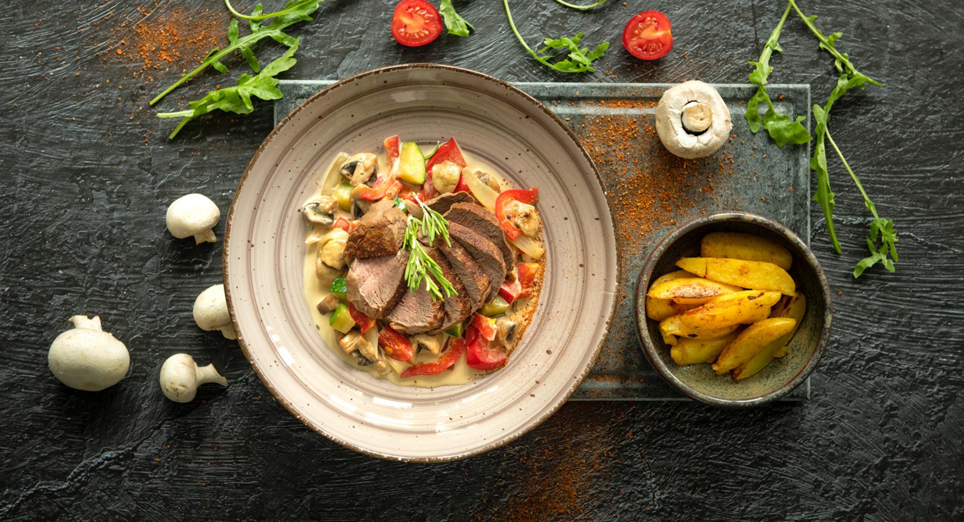 Beef steak on creamy vegetables with potato wedges 