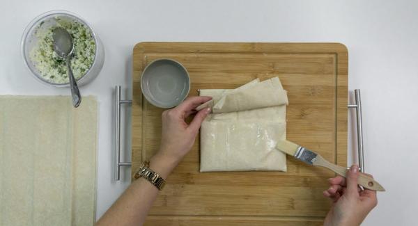 Place 2 sheets of yufka dough on top of each other and spread some Feta mixture on top. Fold the top and bottom sides in the middle. Fold over the right side, lay the left side over it and fix it with a little water.